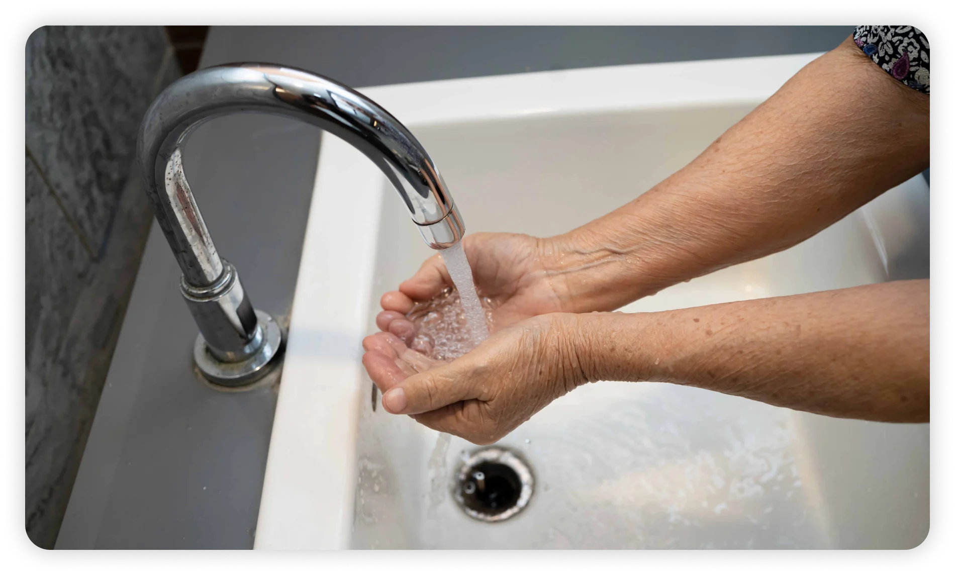 Hands rinsing under running water from a bathroom faucet