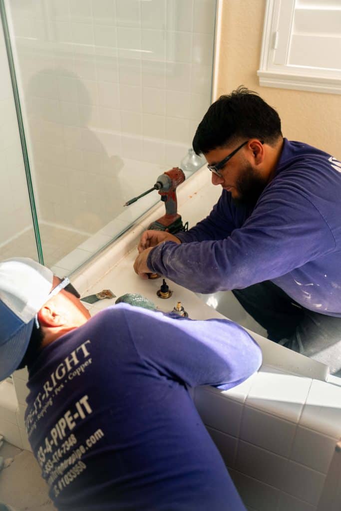 Two plumbing technicians replacing a bathtub water spout